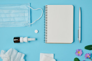 Flat lay concept of seasonal spring and summer pollen allergy with napkins, pills, face mask, pen, notepad, drops bottle and fresh flowers on blue background. Copy space, minimal style, template text