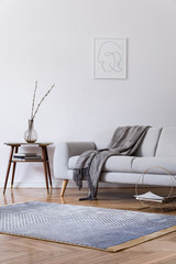 Stylish scandi interior of home space with design grey sofa and retro small table. Living room with...