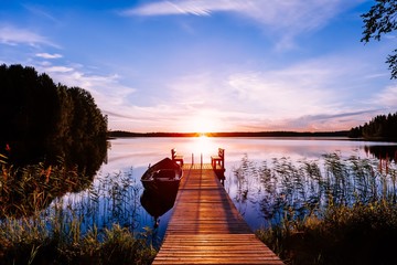 Jetée en bois avec bateau de pêche au coucher du soleil sur un lac en Finlande