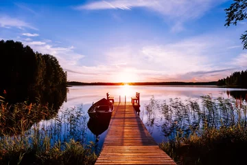 Tuinposter Houten pier met vissersboot bij zonsondergang op een meer in Finland © nblxer