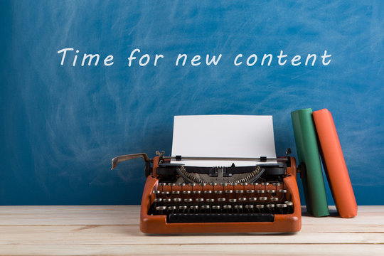 writer's workplace - red typewriter and stationery on blue blackboard background with text "Time for a new content"