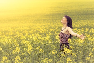 Fototapeta premium Happy beautiful woman in free summer love of youth wellbeing. Attractive young beauty girl enjoying the warm sunny sun in nature rapeseed field takes time feeling sustainability and contemplation