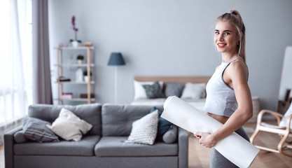 Woman with yoga mat in living room at home.