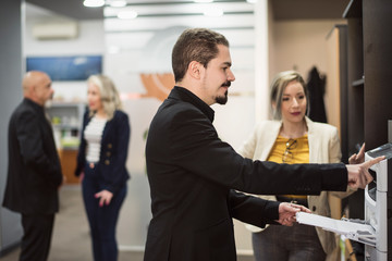 Man in office sending fax or printing files with people in background