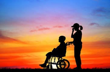 Fototapeta premium silhouette Daughter to care a wheelchair mother to walk on