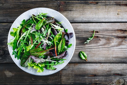 Mix of fresh leaves with arugula, lettuce, beets. Ingredients for salad on a wooden background.