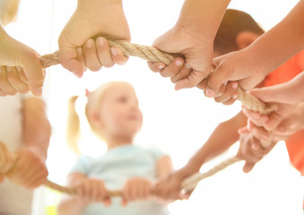 Little children holding rope on light background, focus on hands. Unity concept