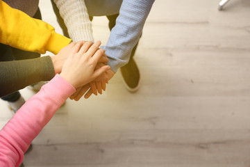 Group of volunteers putting their hands together indoors, closeup. Space for text