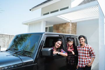 family with kid sitting in a car in car port of their house ready to go