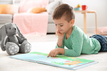 Obraz na płótnie Canvas Little boy with toy reading book on floor at home