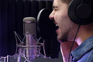 Young singer with microphone recording song in studio