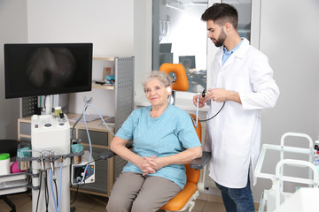 Professional otolaryngologist examining senior woman with endoscope in clinic. Hearing disorder