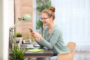 Pretty teenage girl using mobile phone at table in room