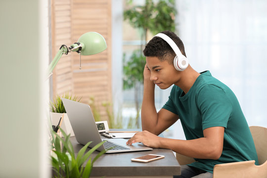 African-American teenage boy with headphones using laptop at table in room