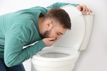 Young man suffering from nausea over toilet bowl indoors