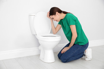 Young woman suffering from nausea at toilet bowl indoors. Space for text