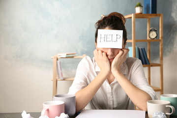 Young woman with note HELP on forehead at workplace. Space for text - obrazy, fototapety, plakaty