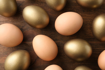 Golden eggs among others on wooden background, flat lay