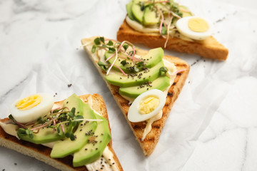 Tasty toasts with avocado, quail eggs and chia seeds on marble background