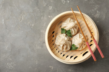 Bamboo steamer with tasty baozi dumplings and chopsticks on grey background, top view. Space for...