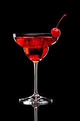 Red cocktail in a glass with cherry in front of black background