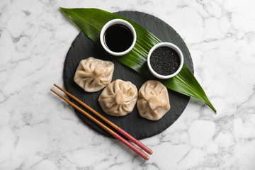 Slate plate with tasty baozi dumplings, chopsticks, sesame seeds and soy sauce on marble table, top...