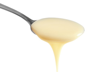 Spoon with condensed milk on white background, closeup. Dairy product