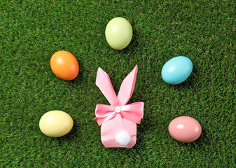 Flat lay composition of Easter bunny gift bag and dyed eggs on green grass