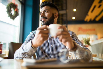 Indian man using laptop computer while drinking a cup hot milk tea, outdoor cafe.