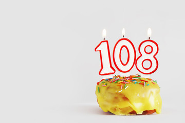 One hundred and eight years anniversary. Birthday cupcake with white burning candles with red...