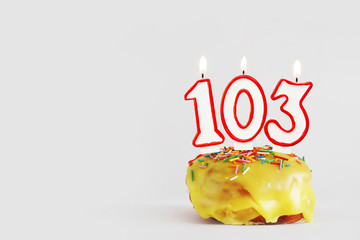 One hundred and three years anniversary. Birthday cupcake with white burning candles with red...