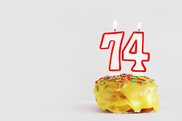 Seventy four years anniversary. Birthday cupcake with white burning candles with red border in the form of 74 number. Light gray background with copy space