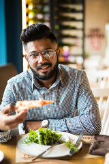 Handsome indian man holding and eat piece pizza and salad in cafe