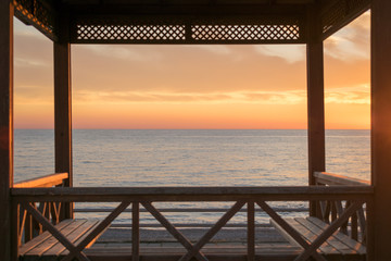 Fototapeta na wymiar Сharming sunset view through cozy gazebo on the beach. Sea horizon. 