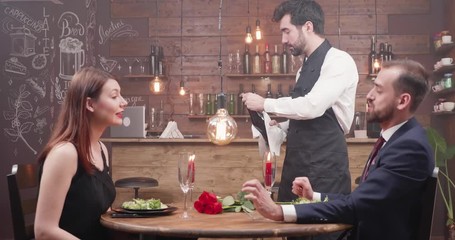Bartender opening a bottle of champagne in front of a couple. Couple on a romanting date ordering champagne.