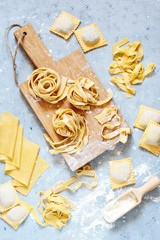 Homemade italian pasta, ravioli, fettuccine, tagliatelle on a wooden board and on a blue...