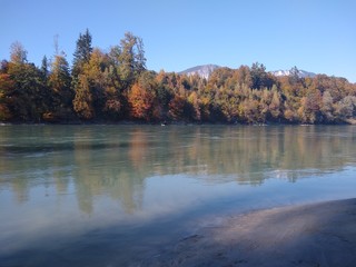 Herbstliches Flussufer in der Abendsonne spiegelt sich im Wasser