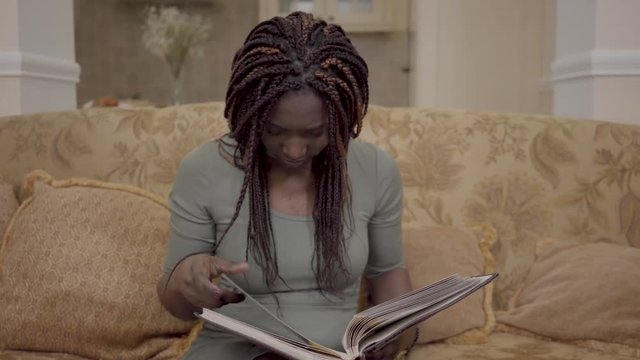 ortrait of cute african american woman with dreadlocks watching the photos in the big leatherback photobook with her bare feet up. Pleasant memories