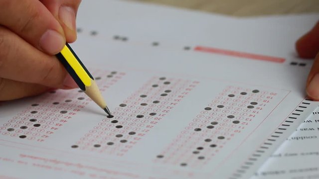 School or university students hands taking exams, writing examination room with holding pencil on optical form answers paper sheet on desk doing final test in classroom. Education assessment Concept