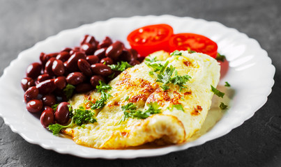 omelet with red beans and tomato in white plate on Dark grey black slate background