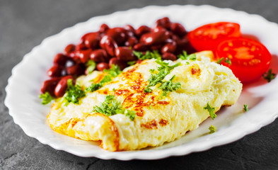 omelet with red beans and tomato in white plate on Dark grey black slate background