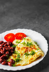 omelet with red beans and tomato in white plate on Dark grey black slate background