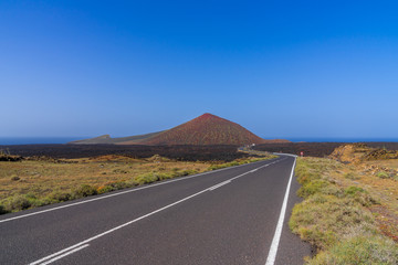 Spain, Lanzarote, Highway alongside red volcano mountain to blue ocean on holiday island