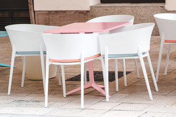 Fototapeta na wymiar Empty coffee and restaurant terrace with pink table and white chairs. Cafe in the street. Summer terrace in Europe. Open air cafe. Modern cafe terrace outside.