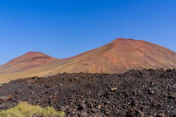Spain, Lanzarote, Two red mountains of volcanic origin behind black lava field