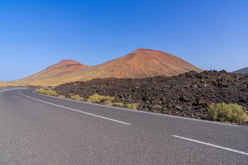 Spain, Lanzarote, Intense red volcano mountains behind curved road on vacation island