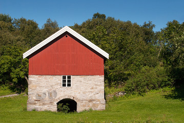 Fototapeta na wymiar Old red wooden barn, with beautiful foundation of natural stones, typical Norwegian, beautiful nature and clear blue sky.