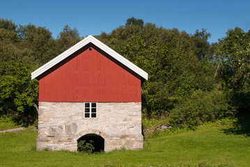 Old red wooden barn, with beautiful foundation of natural stones, typical Norwegian, beautiful nature and clear blue sky.