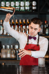 Obraz premium Creative barman making alcoholic drink, pouring fresh cocktail from shaker into matalic glass on the bar stand