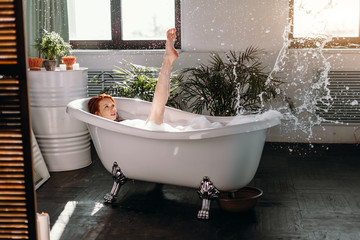 Relaxing woman having fun raises her slim legs in air while taking foam bath at home. Water splash and cheerful mood. Spa and Relaxation concept.